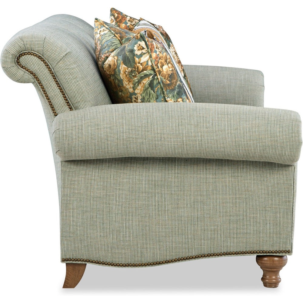 Side view of a green plaid armchair with nailhead trim, wooden legs, and floral throw pillows.