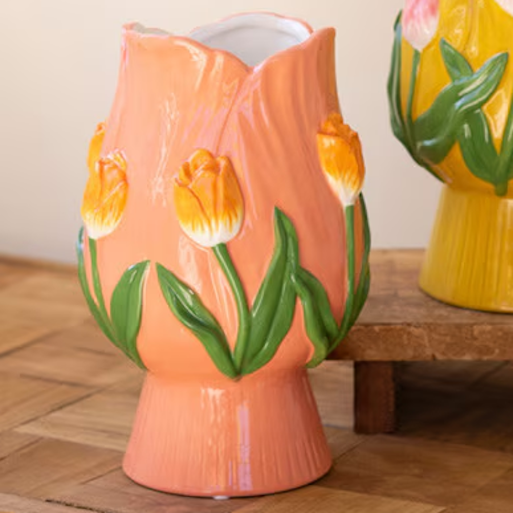 Peach ceramic tulip-shaped vase with embossed orange tulips and green leaves on a wooden surface.