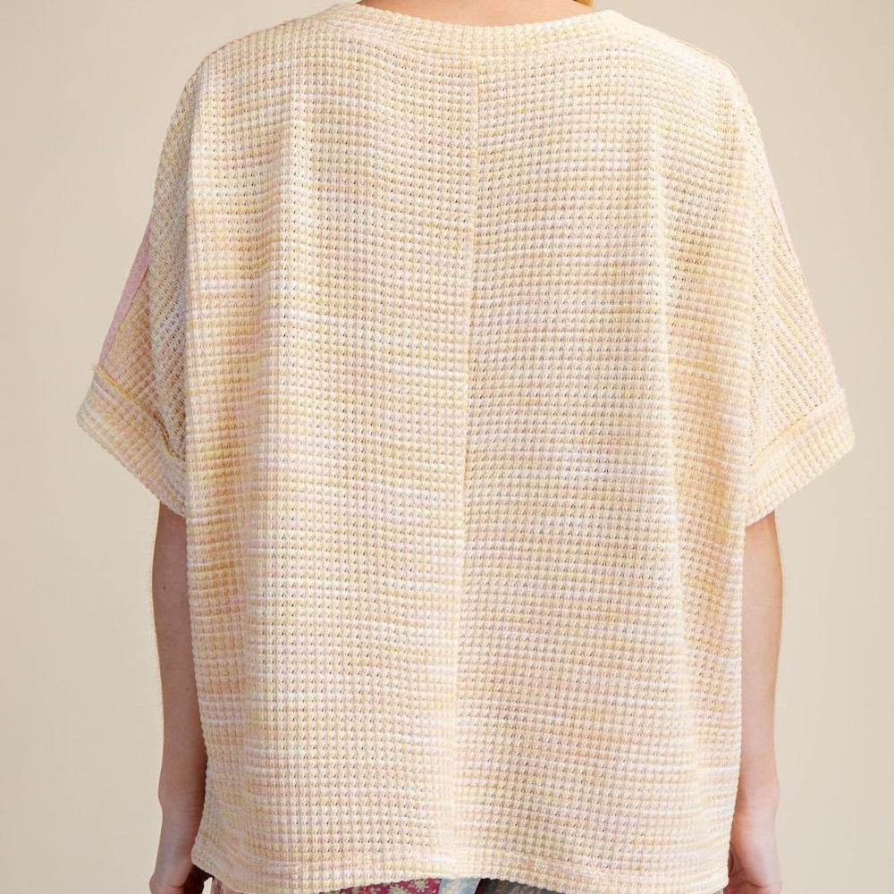 Back view of a peach and lemon yellow waffle-knit oversized top with short cuffed sleeves and central seam detail.