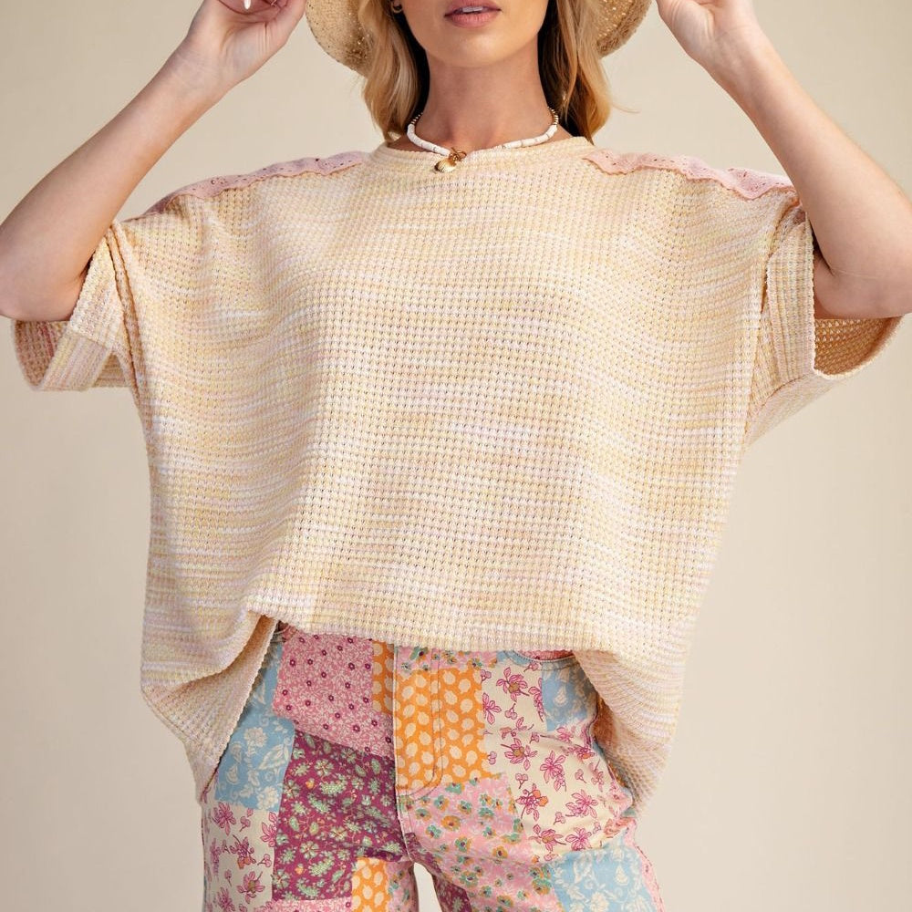 Woman in a peach and lemon waffle knit top with pink eyelet lace shoulders and colorful patchwork floral pants.