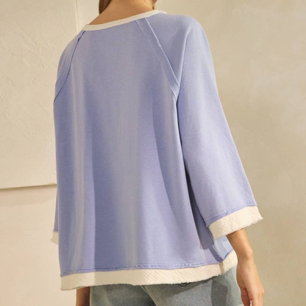 Back view of a periwinkle relaxed Henley-style knit top with white trim and three-quarter sleeves.
