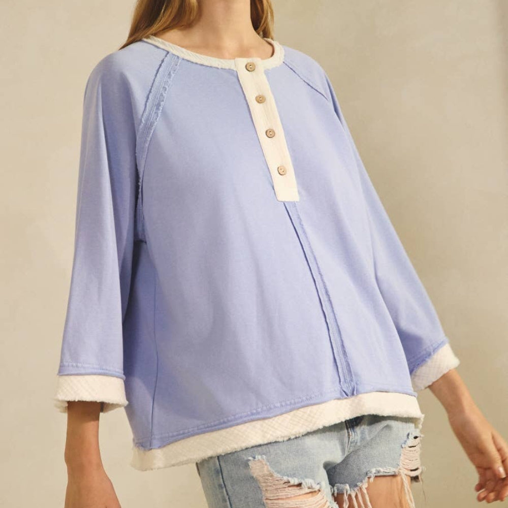 Periwinkle relaxed henley-style knit top with cream trim, button detail, and three-quarter sleeves.