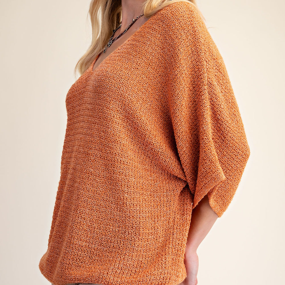 Side profile of a woman wearing a textured burnt-orange V-neck knit sweater with wide 3/4 sleeves.