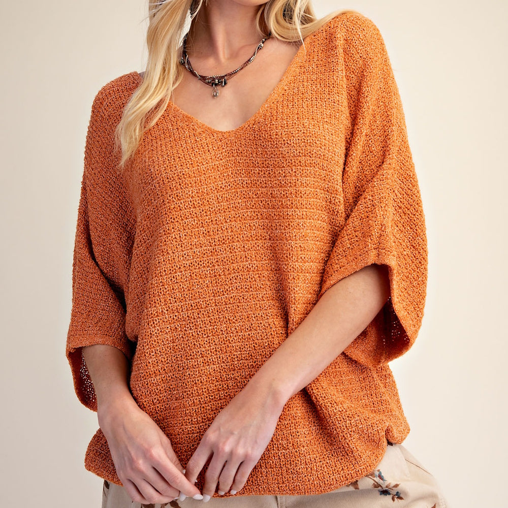 Woman wearing a textured, loose-fitting orange V-neck knit sweater with 3/4 sleeves.