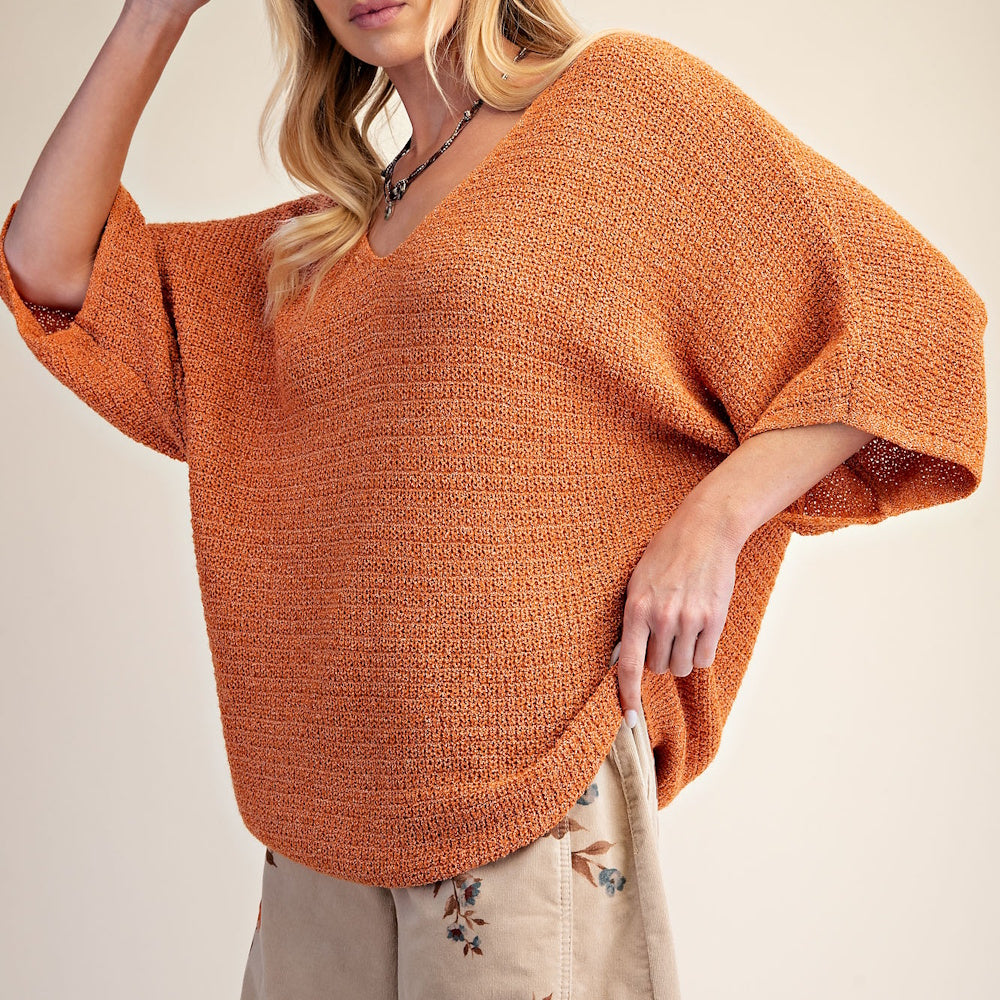 Woman wearing an orange, textured knit v-neck sweater with loose, wide three-quarter sleeves.