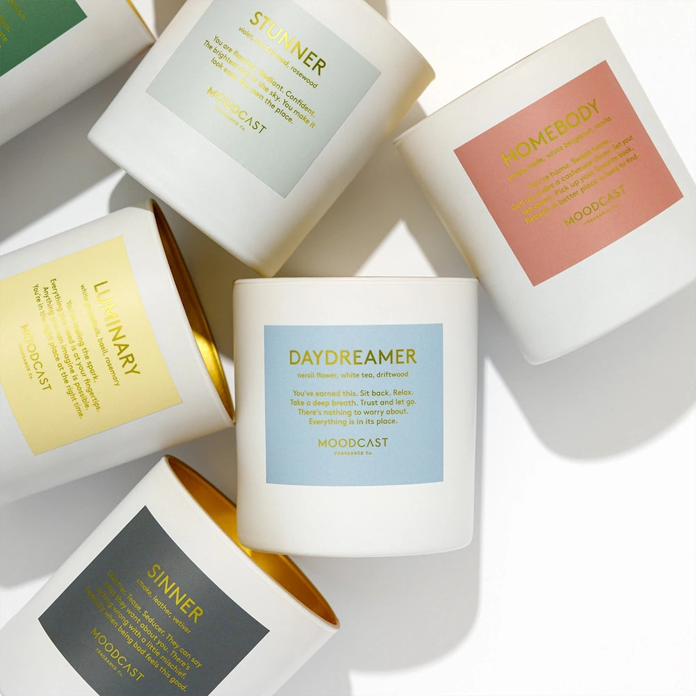 Assorted Moodcast white jar candles with pastel labels including Stunner, Homebody, Luminary, Daydreamer, and Sinner.