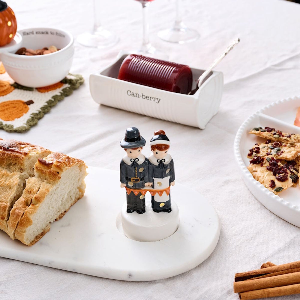 Light-up pilgrim couple decor figurine on a Thanksgiving table next to sliced bread.