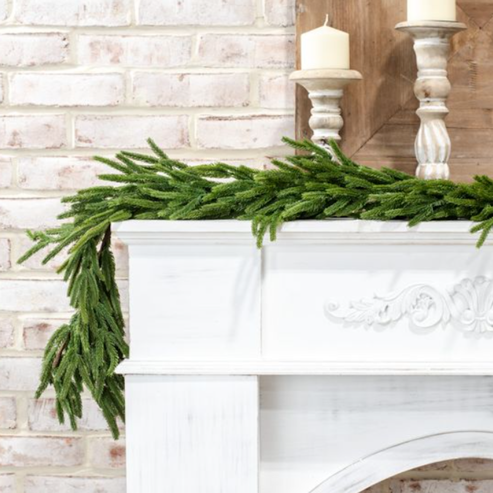 Lush artificial green pine garland draped across a white mantelpiece.