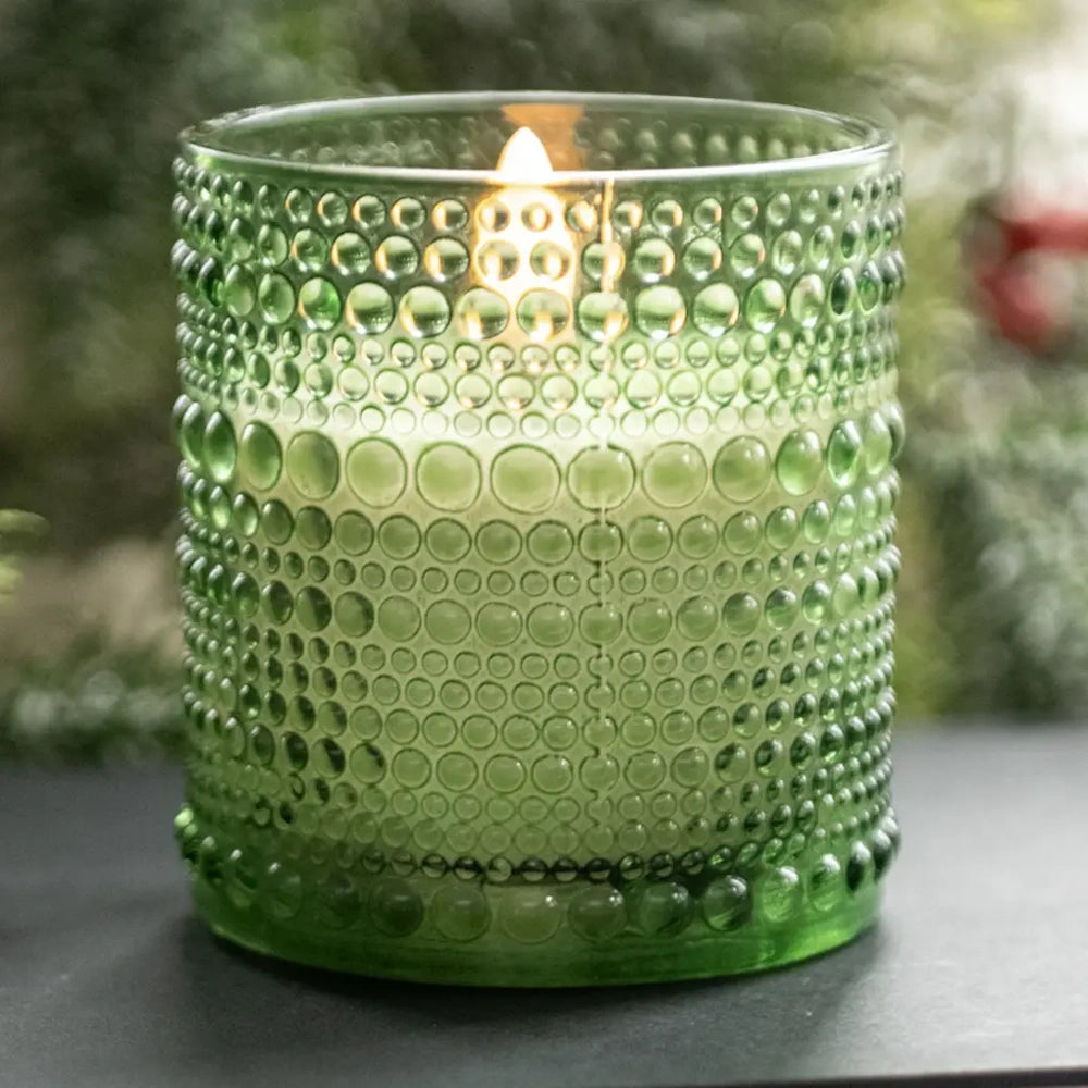 Lit flameless candle in a green hobnail dotted glass holder.