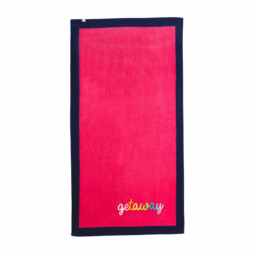 Pink bouclé beach towel with navy blue border and colorful "getaway" embroidery in the corner.