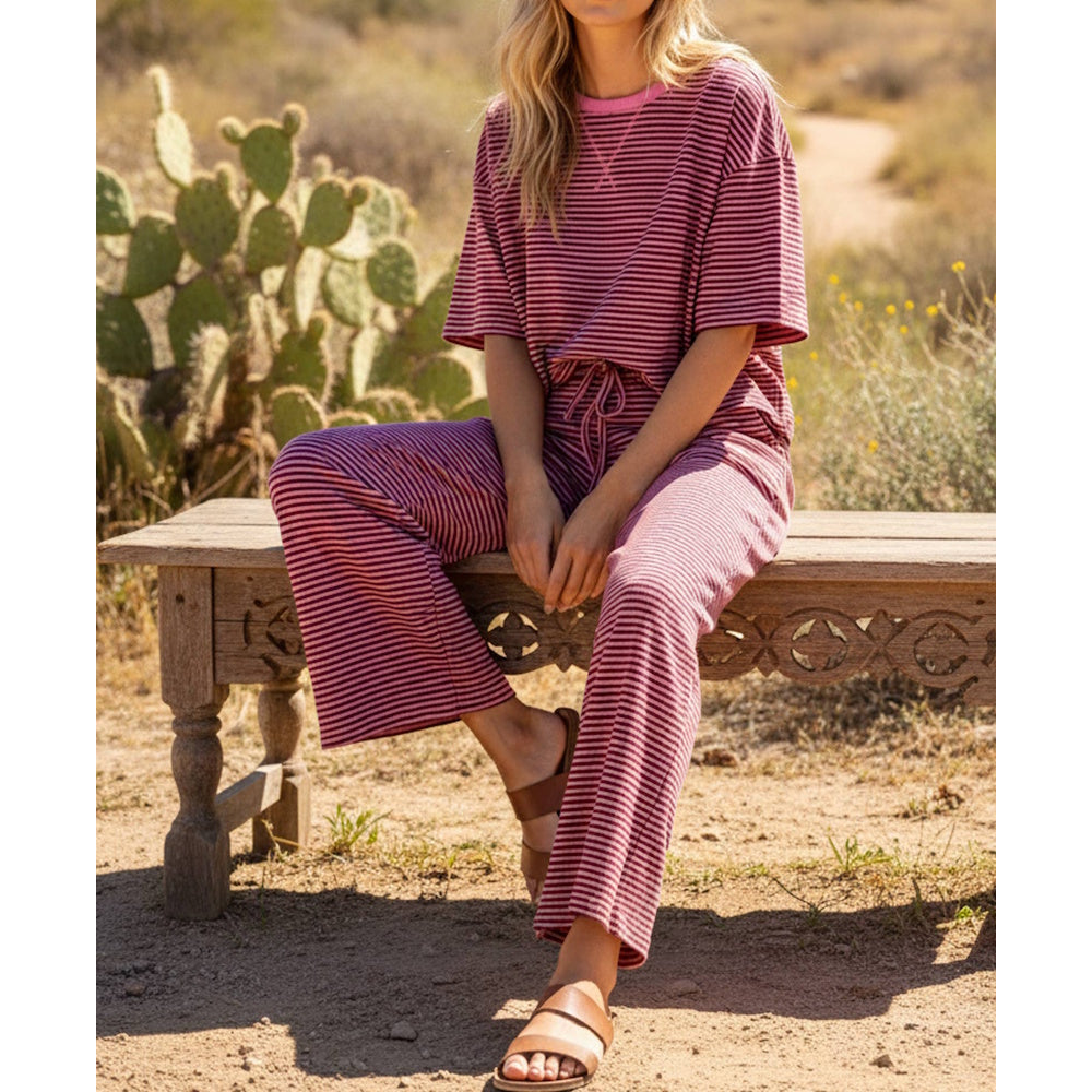 Woman sitting on a wooden bench outdoors, wearing a pink and dark striped knit top and wide-leg pants set.