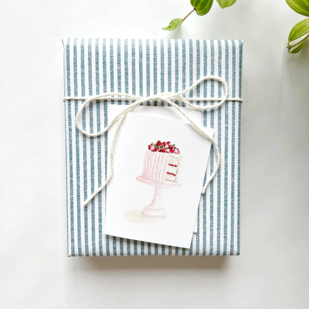 Wrapped gift with blue striped paper, white string bow, and a pink cake card attached.