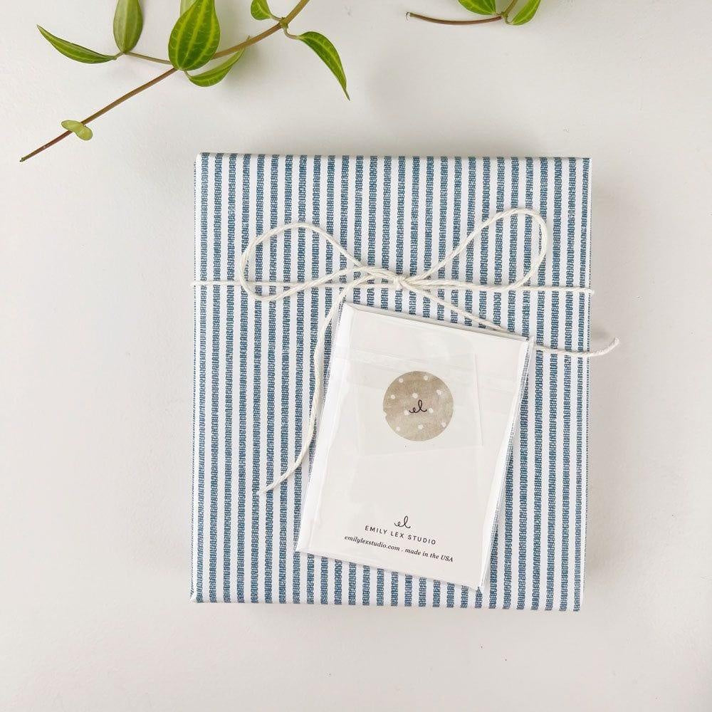 Back of packaged stationery card tied with string onto blue striped gift wrap.