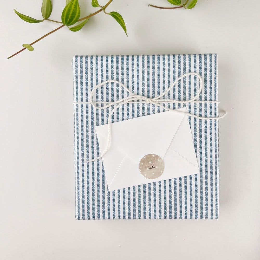 Small white envelope sealed with a round logo sticker, tied to a blue striped gift package.
