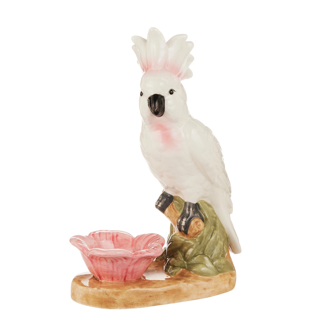 Ceramic figurine of a white cockatoo with pink accents and a raised crest, perched on a base beside a pink flower-shaped dish, conveying elegance.