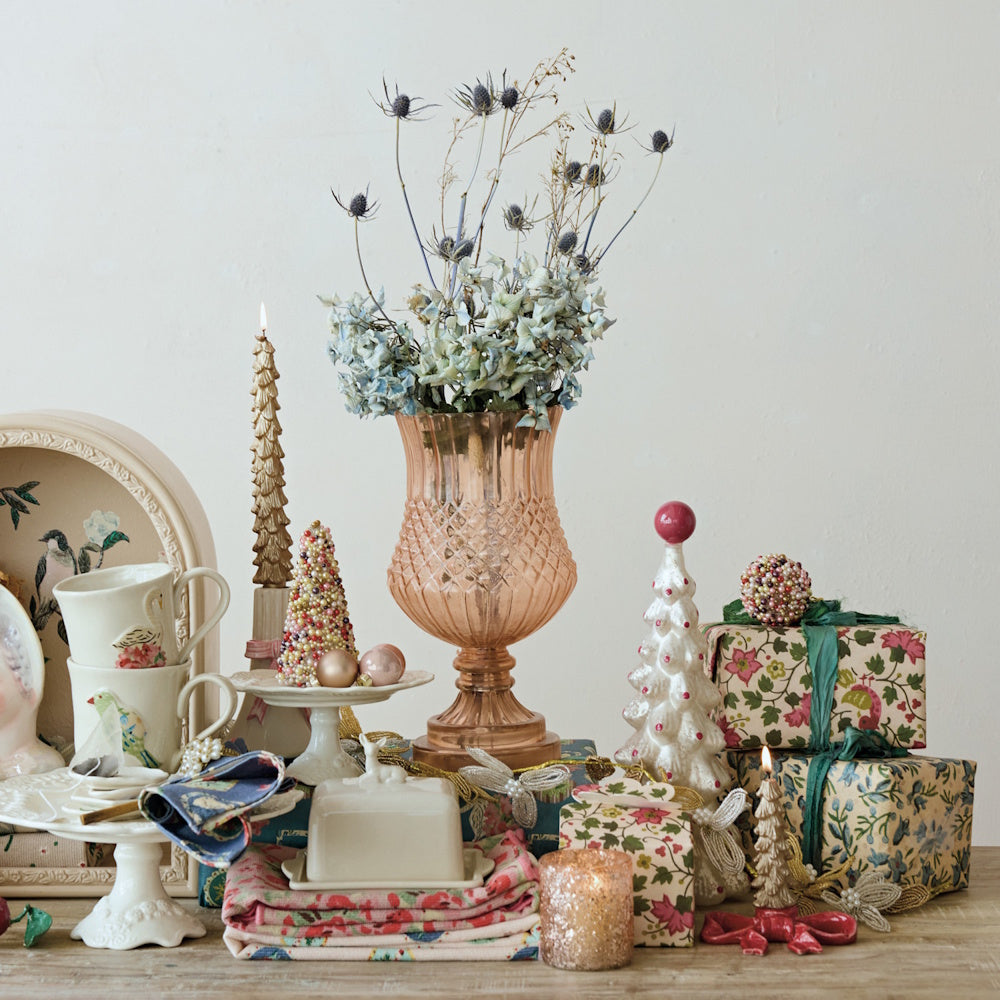 Pink embossed glass footed vase with dried blue flowers, set among festive decor and wrapped gifts.