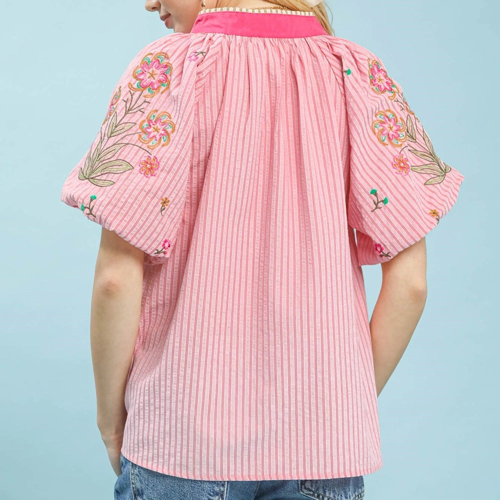 Back view of a pink striped puff-sleeve top with floral embroidery on the shoulders and a bright pink collar.