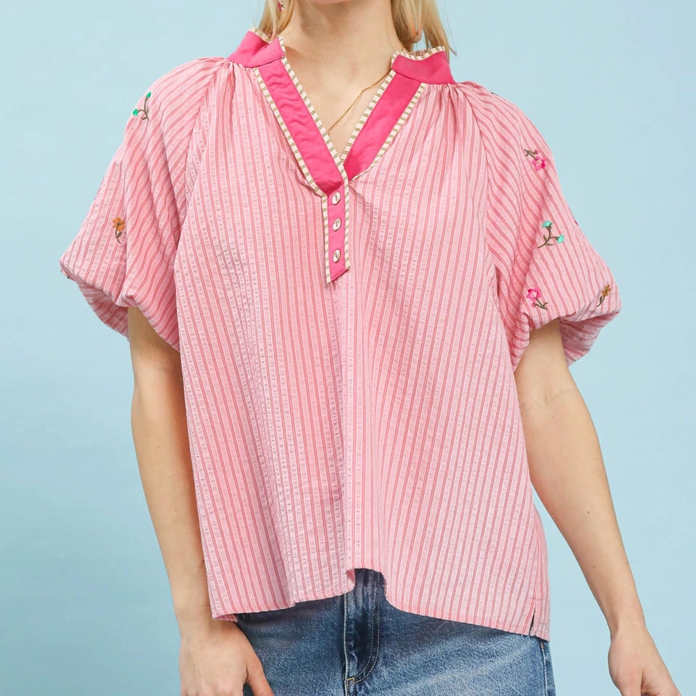 Pink striped V-neck top with embroidered floral sleeves, puff sleeves, and a bright pink collar against a blue backdrop.