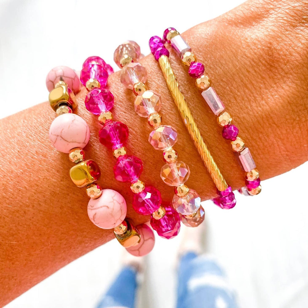 A stack of five beaded and metallic bracelets in shades of pink and gold worn on a person's wrist.