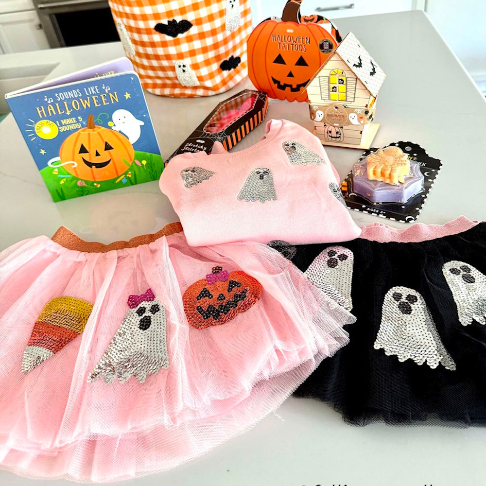 Halloween flat lay with pink and black sequined ghost tutus, a pink sweatshirt, and spooky children's items.