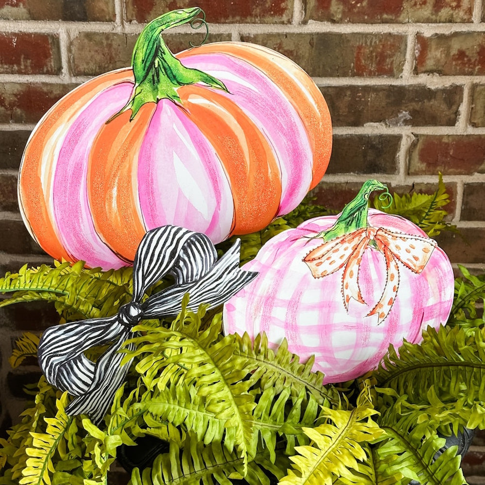 Pink and orange striped pumpkin decor with a gingham pink pumpkin and black and white bow in greenery.