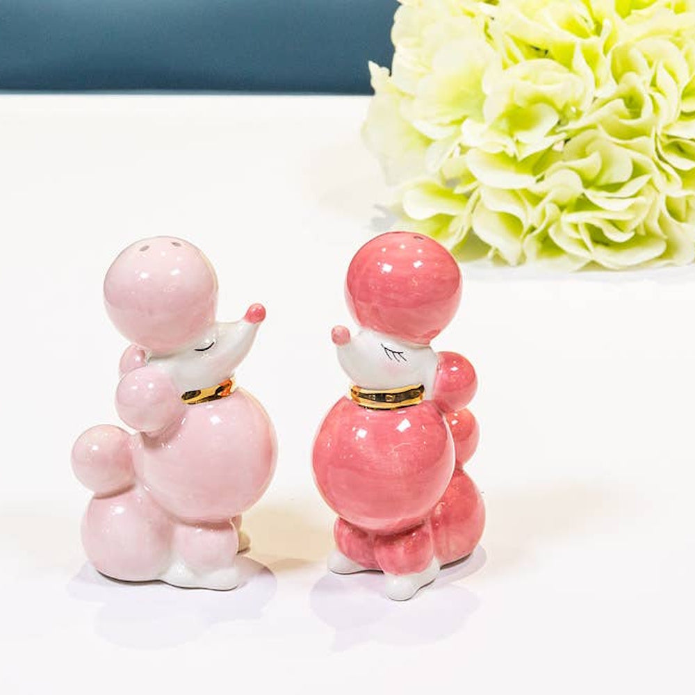 Pink and dark pink ceramic poodle salt and pepper shakers with gold collars on a white tabletop.