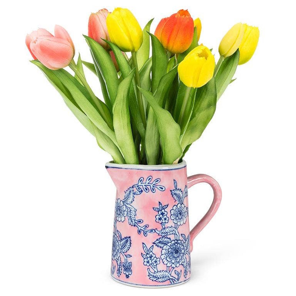 Pink ceramic jug with blue floral pattern holding a bouquet of yellow, orange, and pink tulips.