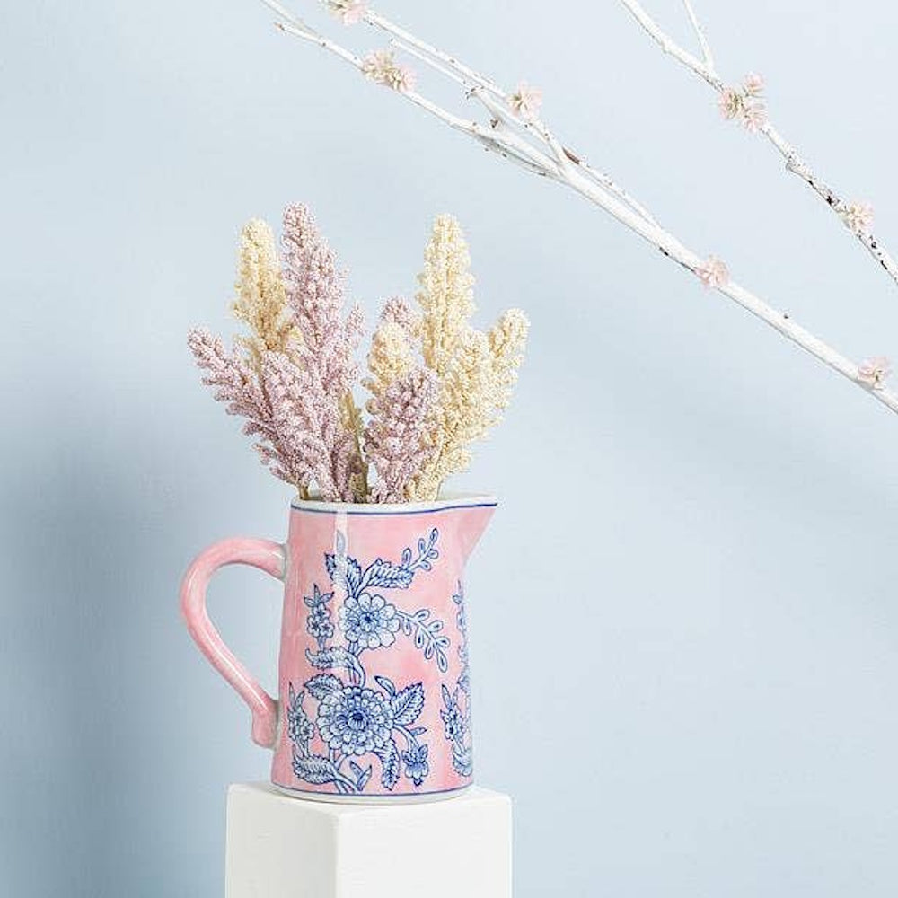 Pink floral ceramic jug with blue chintz pattern holding dried flowers on a white pedestal.