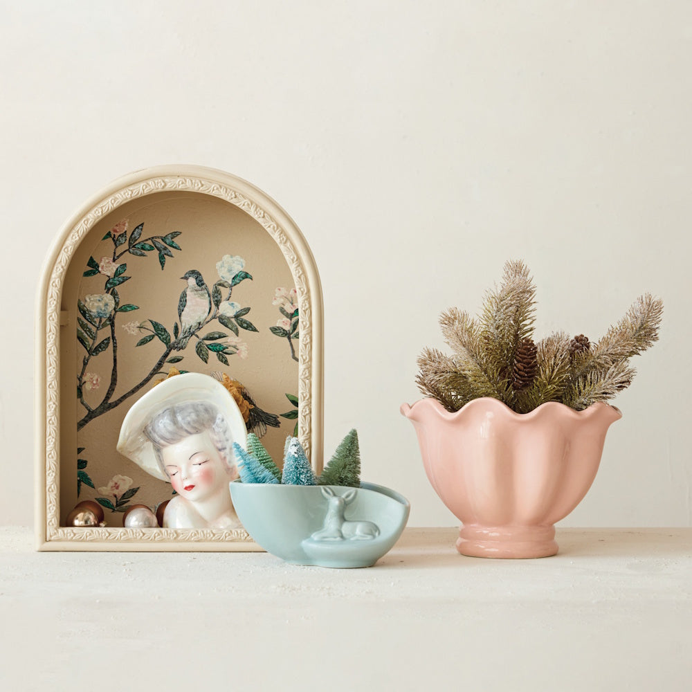 Pink ruffled footed bowl with pine branches beside vintage decor and a small blue planter.