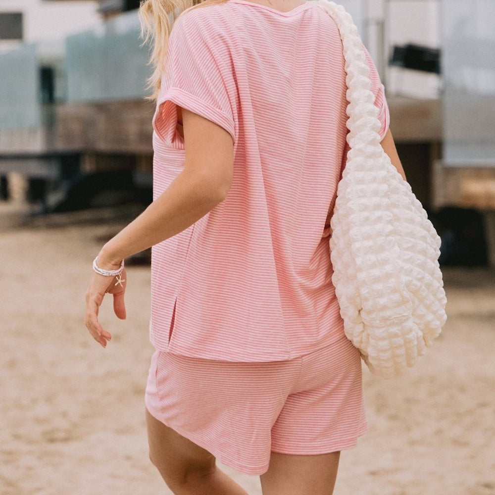 Rear view of a woman walking on sand wearing a pink and white striped matching t-shirt and shorts set.