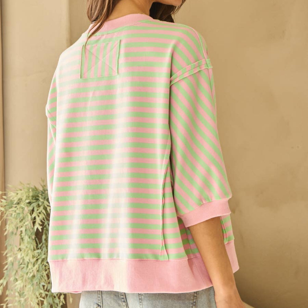 Back view of a woman wearing a pink and green horizontal striped knit top with three-quarter sleeves and a ribbed hem.