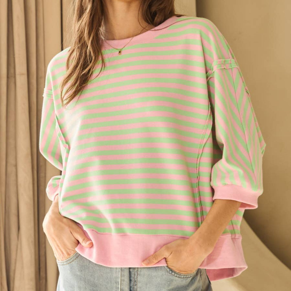 Woman wearing a pink and green horizontal striped knit top with three-quarter sleeves and a relaxed fit.
