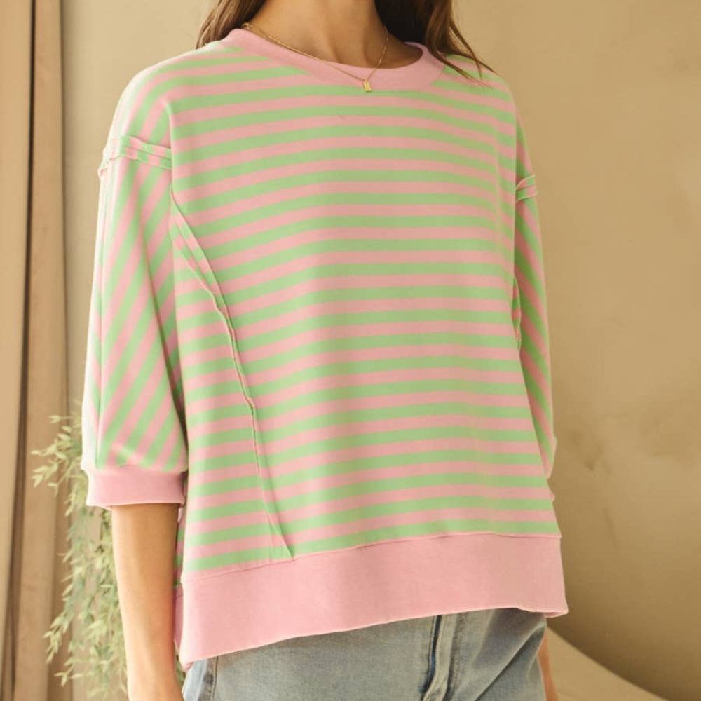 A person wearing a pink and green horizontal striped knit top with short sleeves and a wide pink hem.