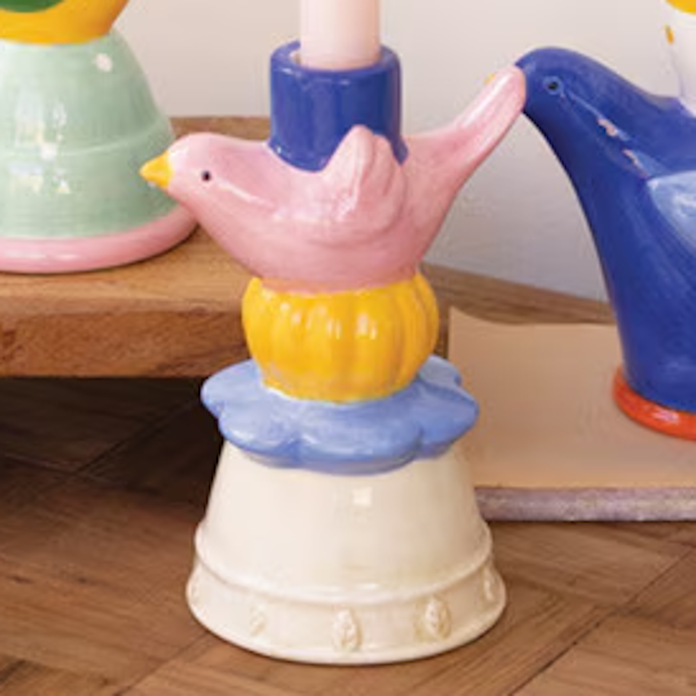 Colorful ceramic bird taper candle holder with a pink bird, yellow and blue accents, and a cream-colored base.