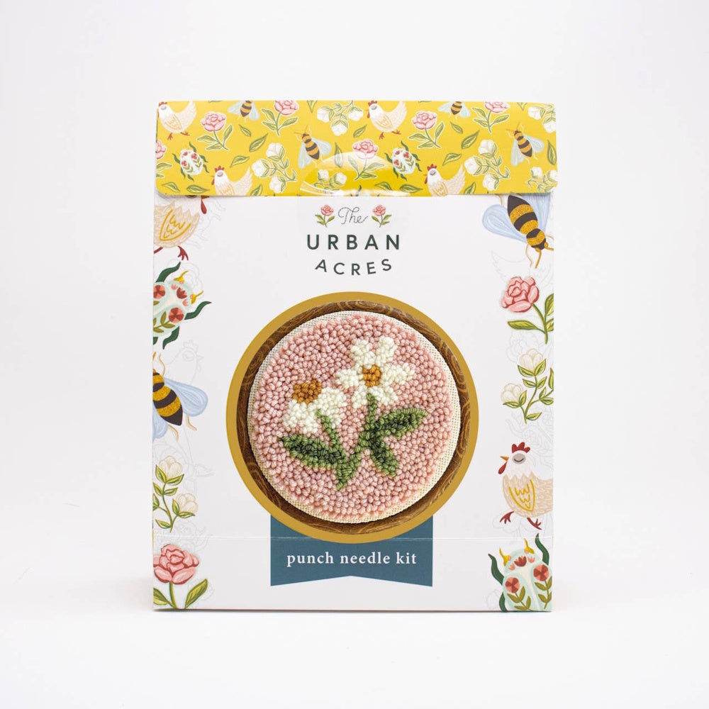 Punch needle kit box featuring a floral design of white daisies on a textured pink background.