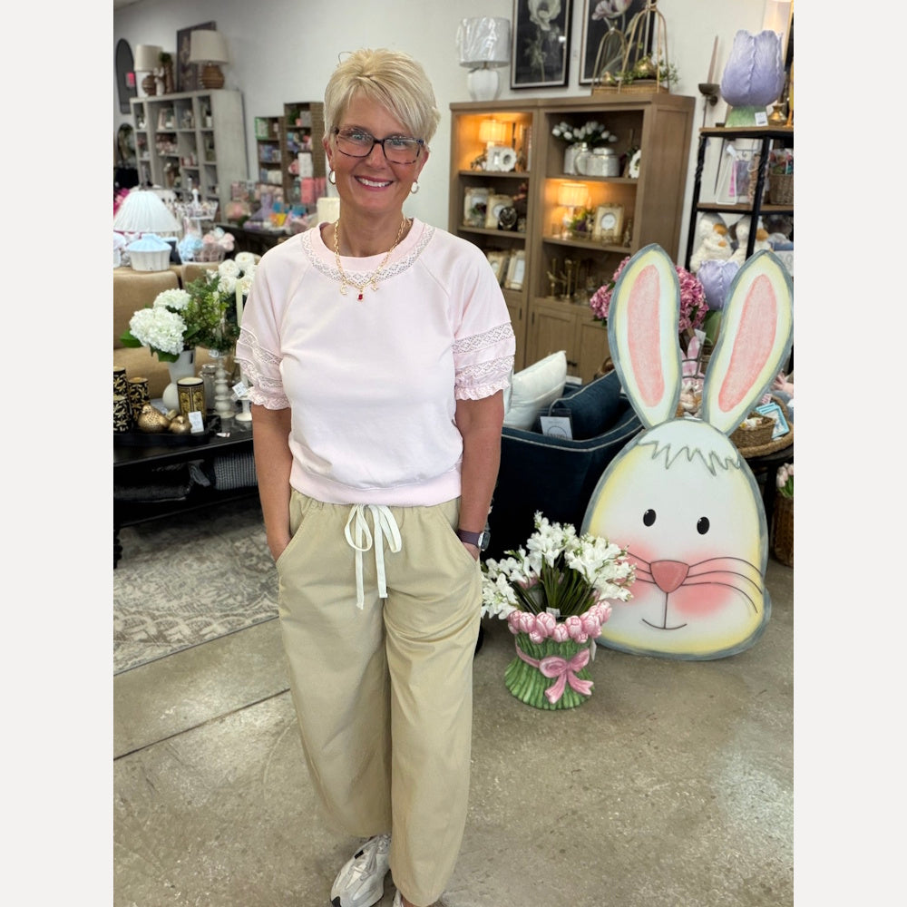 Woman in a pink lace puff sleeve top and khaki drawstring pants posing in a home decor store with Easter bunny decor.