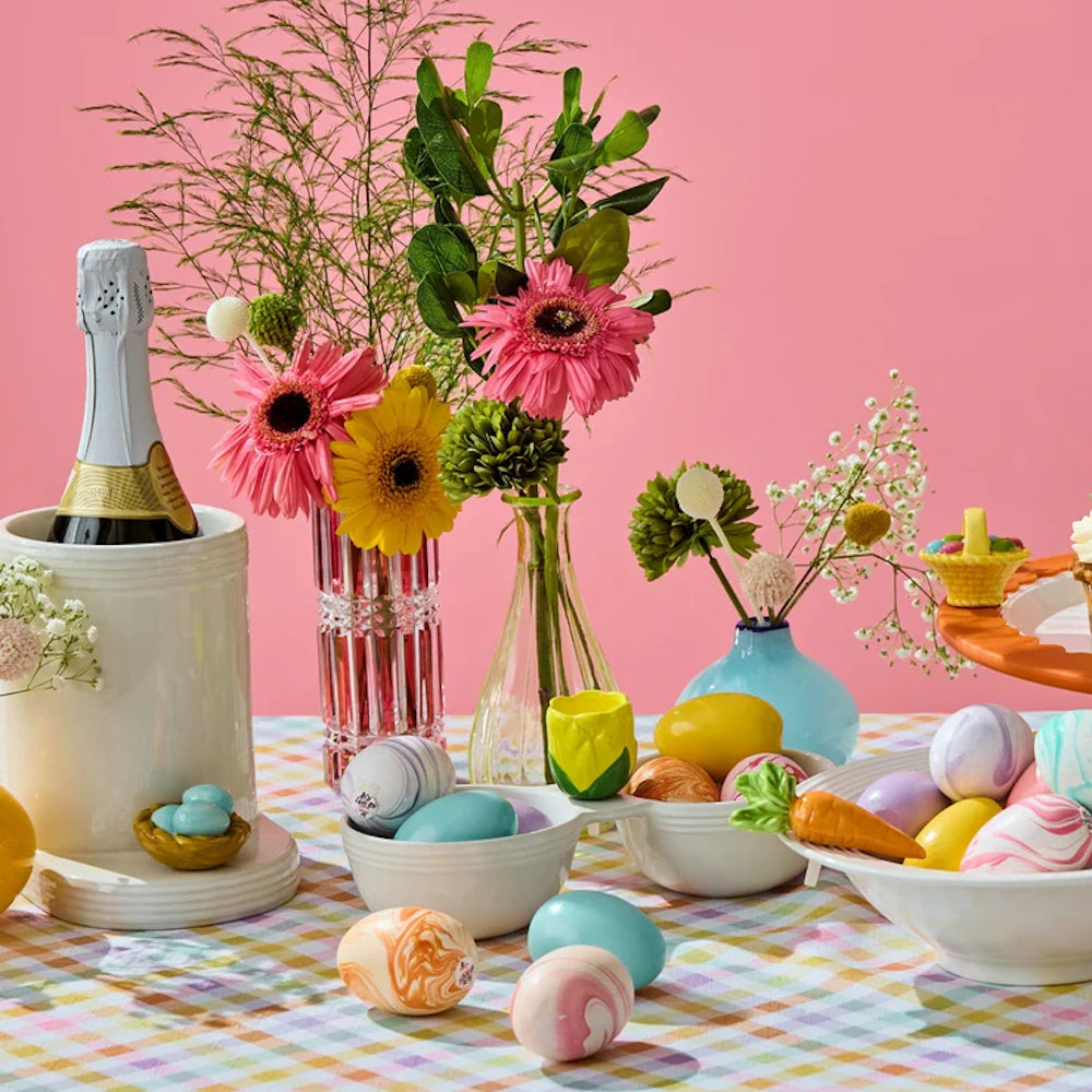 A bright Easter table setting with pastel marble eggs, vibrant flowers, a ceramic carrot, and wine.