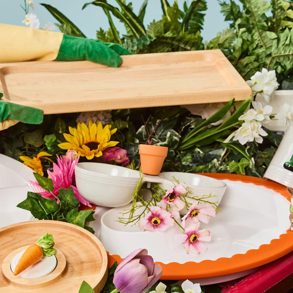 Garden-themed display with white serving bowls, a wooden tray, a ceramic carrot mini, and faux flowers.