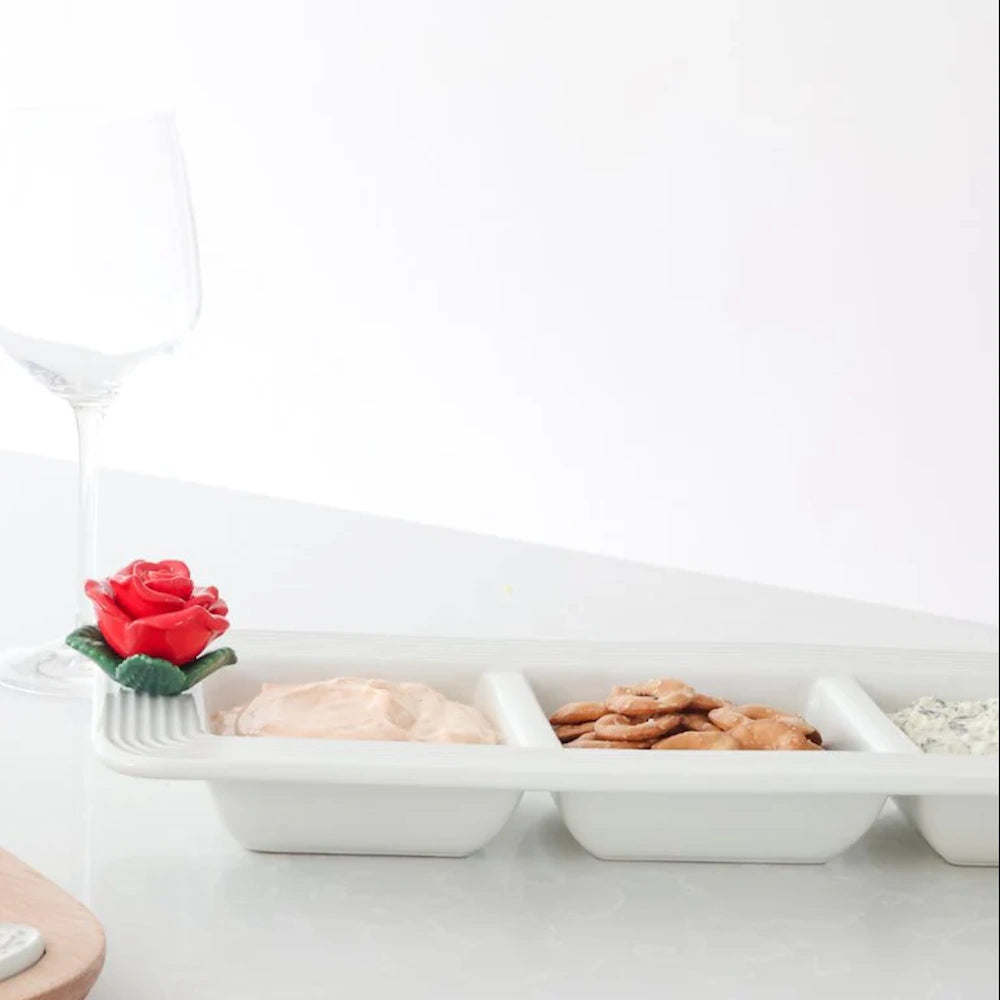 Divided white dish holding dips and pretzels, featuring a small ceramic red rose on the rim.