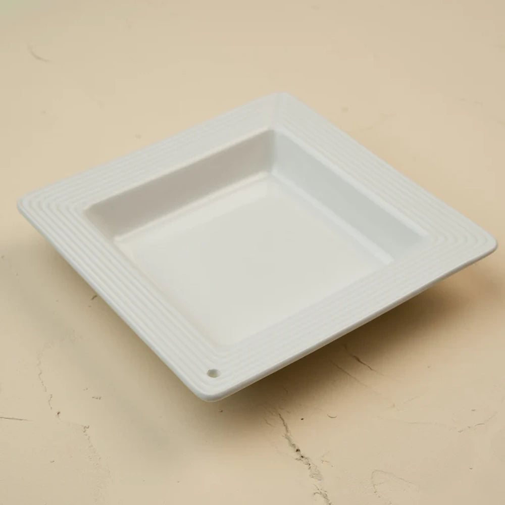 Square white ceramic dish with a pinstripe textured rim and a small hole in one corner.