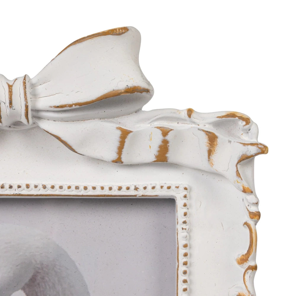 White vintage-style photo frame with ornate bow detail and distressed gold accents on an off-white textured border.
