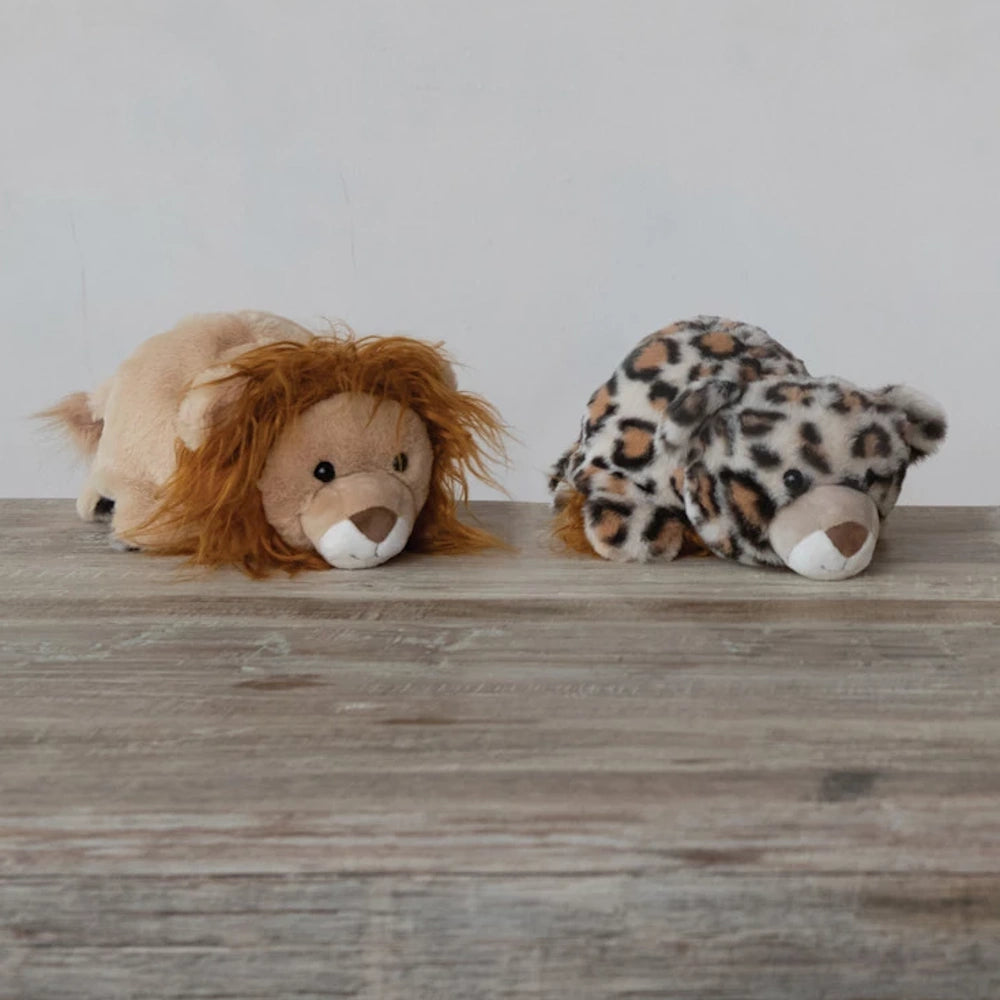 Plush lion and leopard stuffed animals lying on a wooden surface against a neutral background.