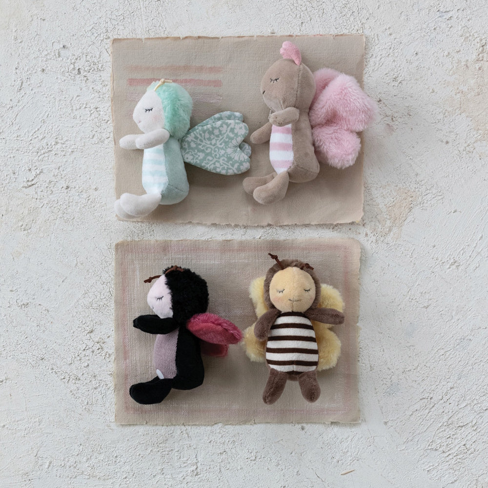 Four small, cute stuffed plush bug toys arranged on fabric mats over a textured white background.