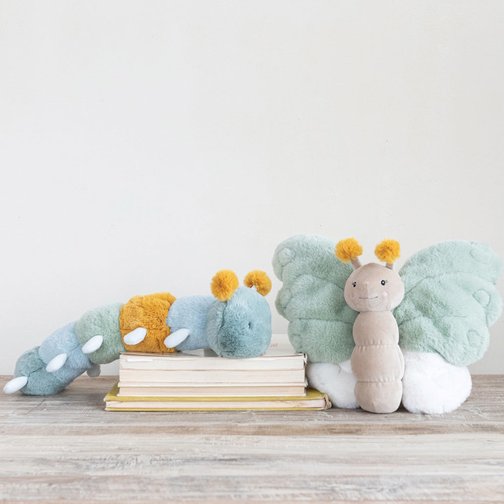 Two plush toys, a multi-colored caterpillar resting on books and a winged butterfly, on a wooden surface.