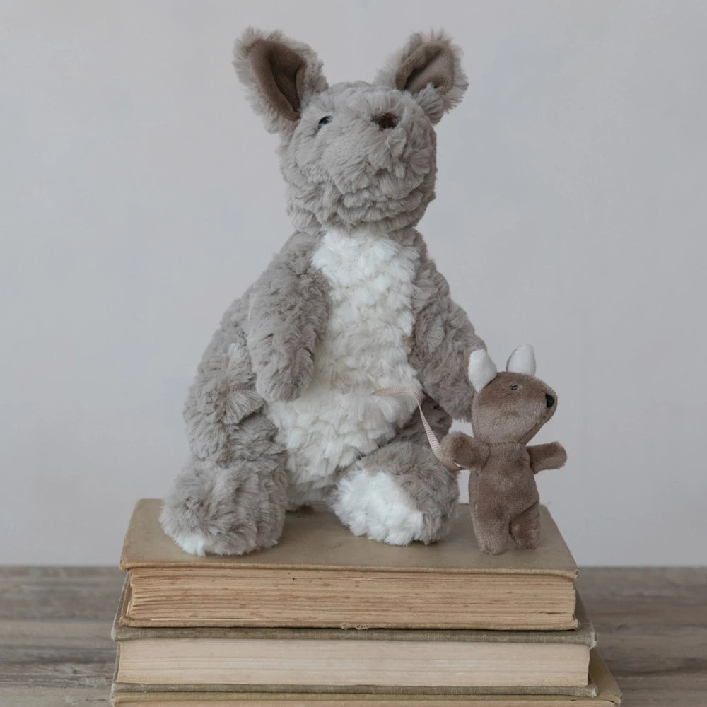 Plush grey and white kangaroo toy standing on a stack of vintage books next to a small brown joey stuffed animal.