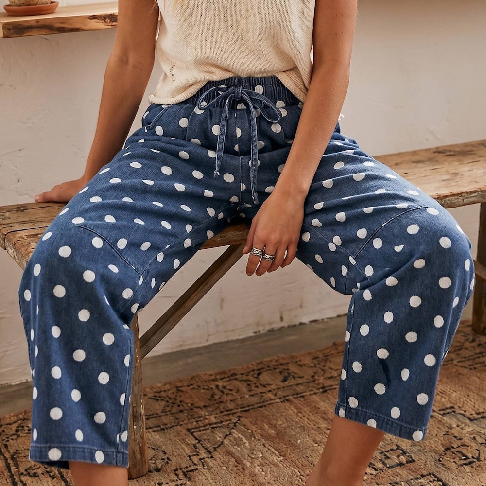 Close-up of a person wearing blue denim polka dot drawstring pants while sitting on a wooden bench.