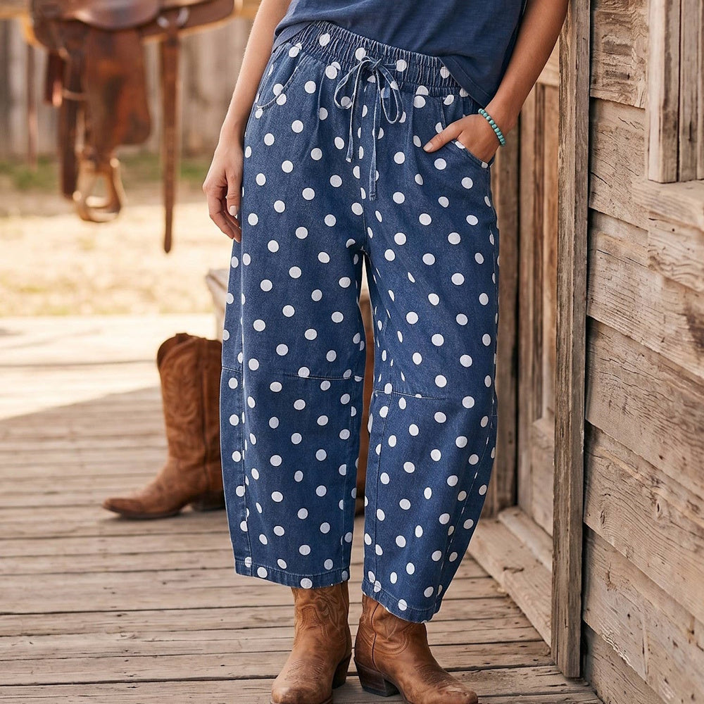 Woman wearing blue polka dot barrel pants with drawstring waist, styled with brown cowboy boots on a wooden porch.