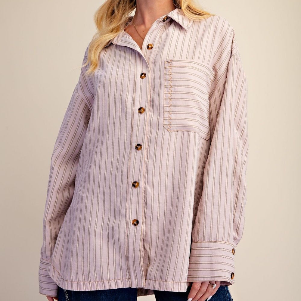 Woman wearing an oversized striped button-down shirt with long sleeves and a chest pocket.