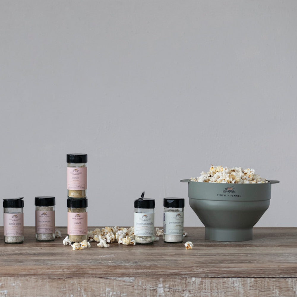 Green silicone popcorn popper bowl next to several small seasoning jars on a rustic wooden table.