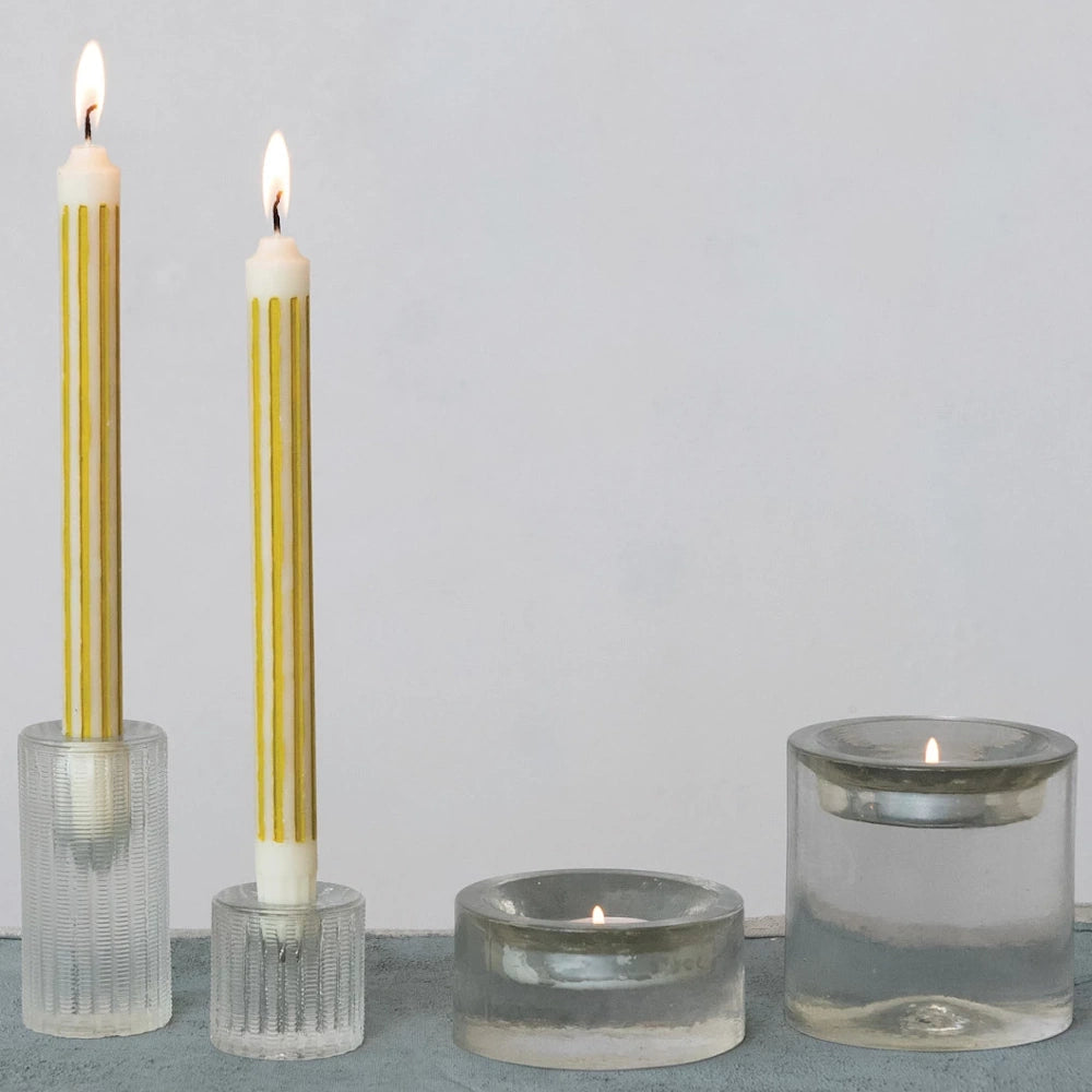 Two lit yellow and white striped taper candles and two tea lights in various clear fluted and smooth glass holders.